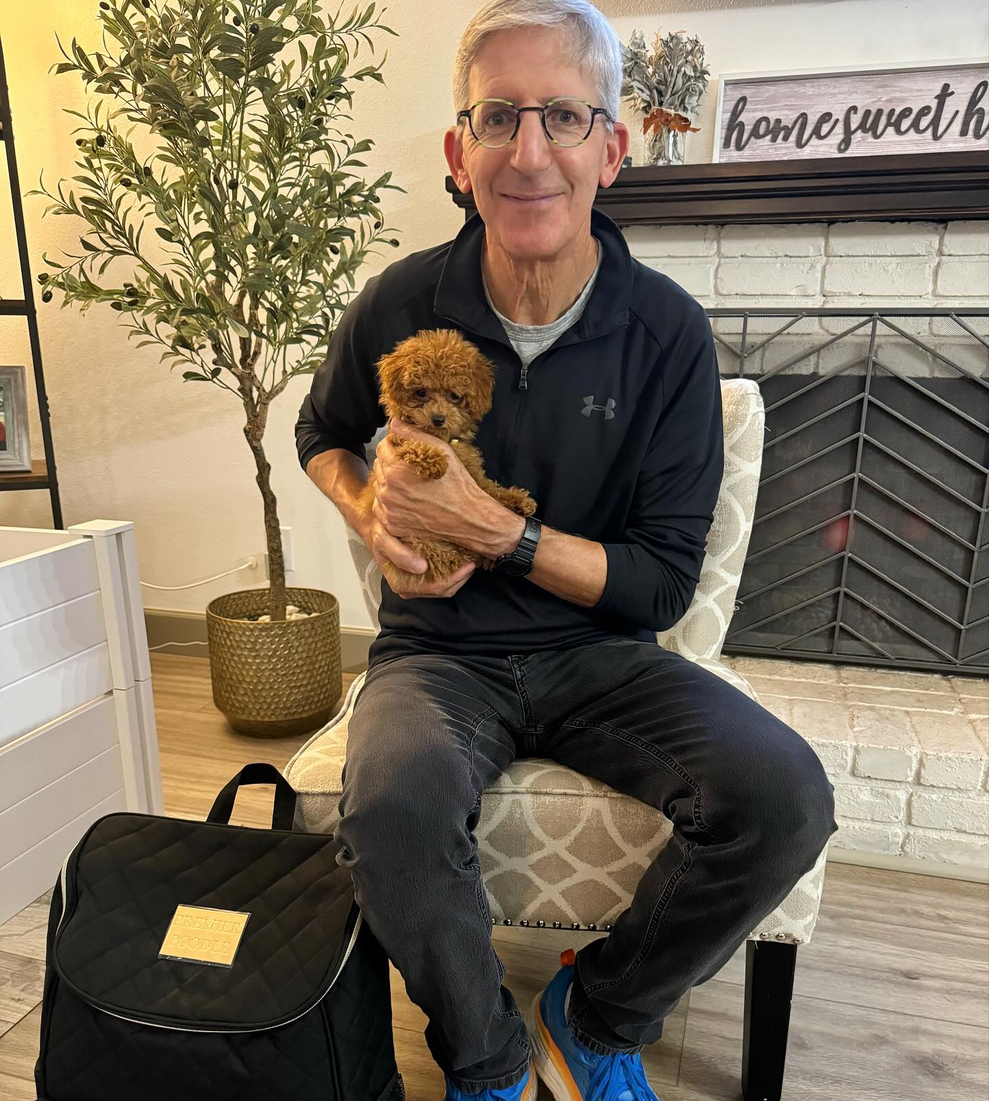 Older man seated indoors holding a small curly puppy