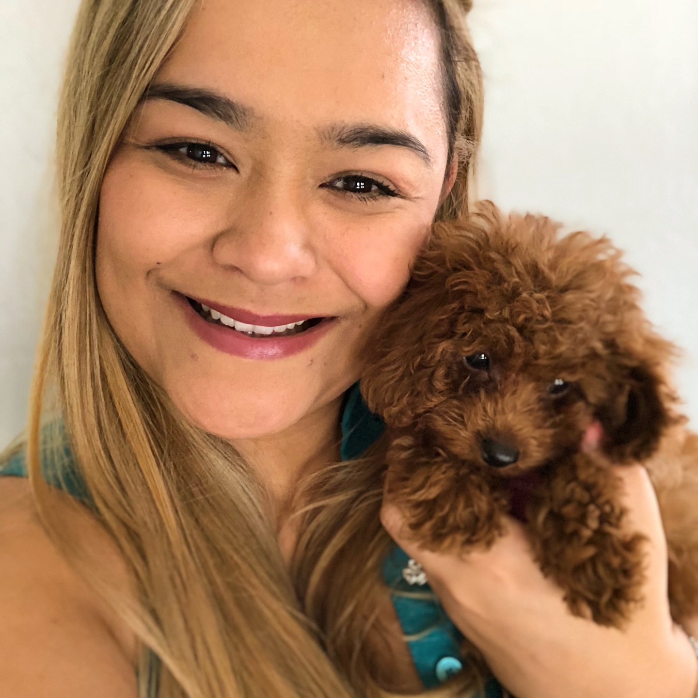 Woman smiling with a small curly brown puppy in a close-up portrait